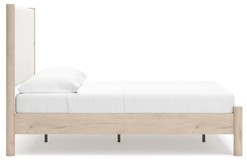 Ashley Furniture Cadmori upholstered bed with beige fabric, padded headboard, and wooden legs, shown from a side angle.