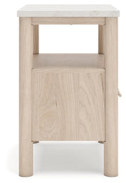 Ashley Furniture Cadmori nightstand with a dark wood finish and sleek design, shown with open drawer and decorative items.