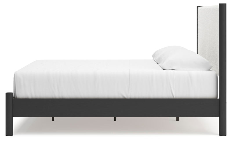 Ashley Furniture Cadmori upholstered bed with tufted headboard and neutral fabric, shown from a side angle.