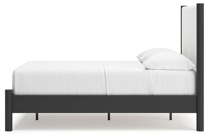 Ashley Furniture Cadmori upholstered bed with a plush headboard and neutral fabric, shown from a side angle.
