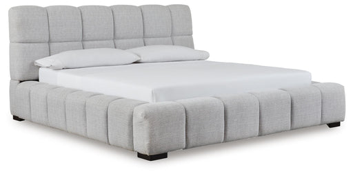 Ashley Furniture Grendusk upholstered bed with a tall padded headboard and neutral fabric, shown from an angled view.