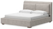 Ashley Furniture Cabalynn upholstered bed with tufted headboard and neutral fabric, shown from a side angle.