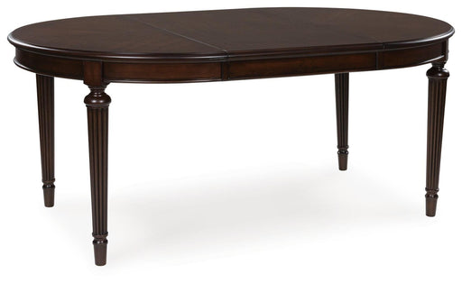 Ashley Furniture Lavinton dining extension table with leaf, shown from an angle with a polished wood finish and sturdy legs.