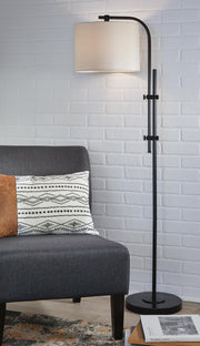 Ashley Furniture Baronvale floor lamp with a sleek metal stand and fabric shade, standing tall in a modern living room setting.
