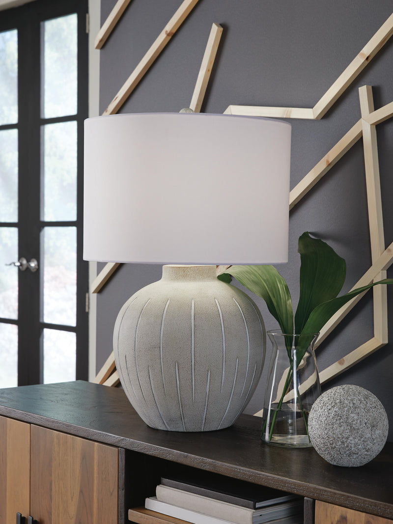Ashley Furniture Calbert Table Lamp with fabric shade and wooden base, shown on a side table in a living room setting.