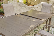Outdoor Ashley Furniture beach front dining table with wooden top and metal legs, set for outdoor dining by the water.