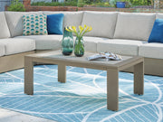 Ashley Furniture Kimpton Isle outdoor cocktail table with a woven rattan design and glass top for patio lounging.