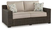 Ashley Furniture Coastline Bay outdoor loveseat with cushion, featuring woven frame and comfortable seating, shown from an angled view.