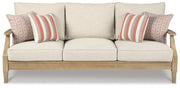 Ashley Furniture Clare View outdoor seating set with cushioned chairs and a glass-top table in a garden setting.
