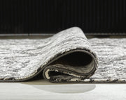 Medium Ashley Furniture Glennisman rug with intricate patterns and warm tones, shown rolled out on a wooden floor.