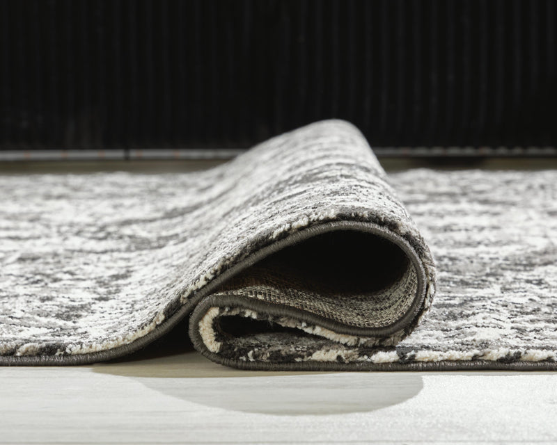 Medium Ashley Furniture Glennisman rug with intricate patterns and warm tones, shown rolled out on a wooden floor.