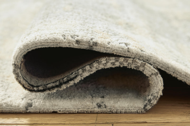 Close-up of Ashley Furniture Raif Rug showcasing intricate woven pattern and soft texture in neutral tones.