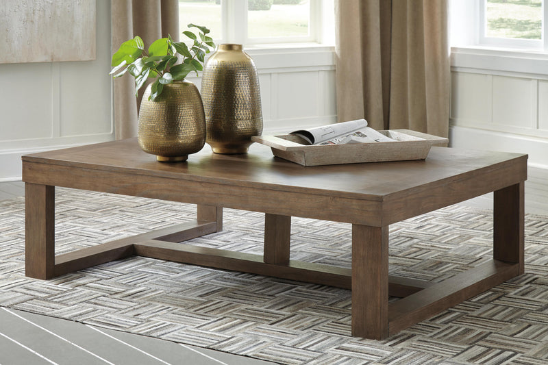 Ashley Furniture Cariton coffee cocktail table with a sleek wooden top and metal frame, shown in a modern living room setting.